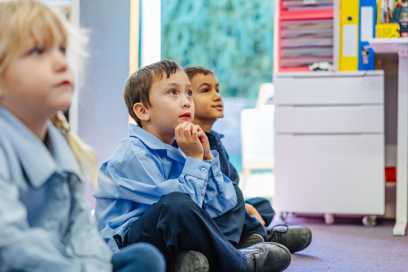 Young students seated on the classroom floor listening attentively at our school near Morisset NSW.