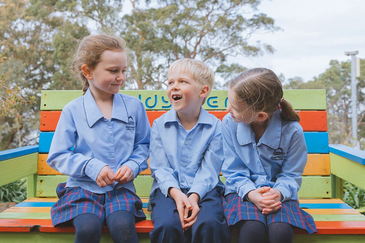 Kindergarten students sitting on sitting on bench surrounded by supportive friends